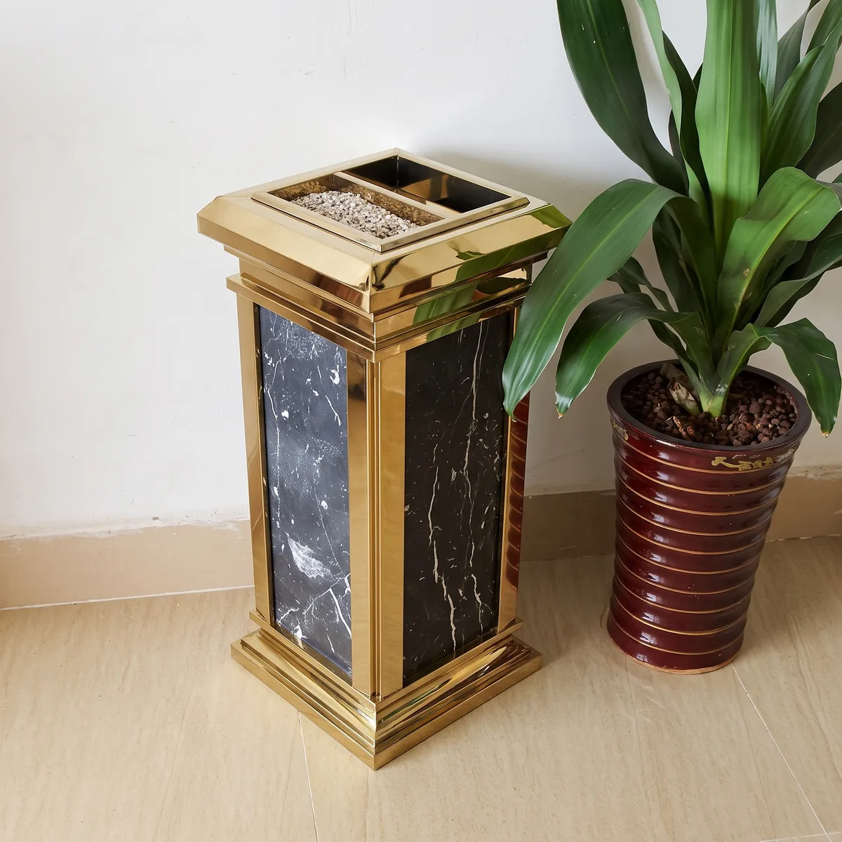 Thùng rác đá hoa cương khung inox vàng đặt cạnh cây trang trí trong sảnh